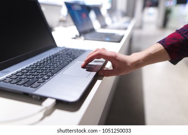 The Man Controls The Computer With A Touchpad. A Man's Hand Uses A Laptop In The Electronics Store. The Buyer Chooses A Laptop In A Technology Store