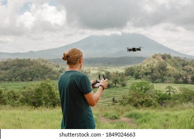 Man controls a quadrocopter in the park, fly over green field in summer park, mountain view