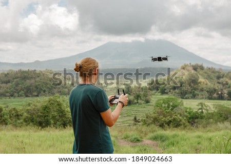 Man controls a quadrocopter in the park, fly over green field in summer park, mountain view