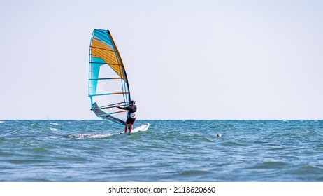 A man controls a sailboard at sea: one of the best remedies for a pandemic is windsurfing, and no mask is needed! - Powered by Shutterstock