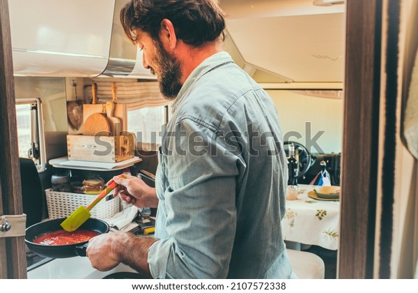 Man cooking in a camper van kitchen\
inside. Holiday travel vacation people lifestyle. Adult caucasian\
male cook tomatoes in motorhome camping car\
interior