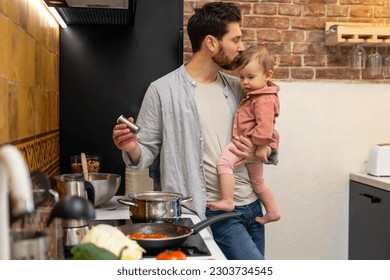 Man cooking dinner with baby daughter in hands standing in kitchenn, father kissing infant baby. - Powered by Shutterstock