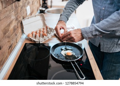 Man cooking eggs for breakfast, standing at the kitchen at home. - Powered by Shutterstock