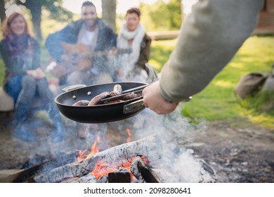 Man cooking hot dogs over campfire for friends - Powered by Shutterstock