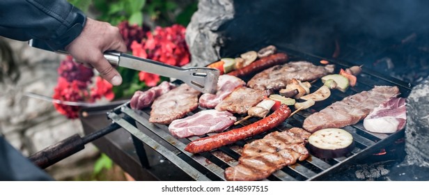 Man Cooking Meat On Barbecue Grill At Bbq Party In Summer Garden. Food, People And Family Time Concept