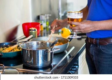 Man Cooking On An Electric Stove In The Kitchen While Drinking A Beer. Preparing Food. Messy Kitchen Counter