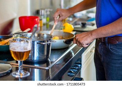 Man Cooking On An Electric Stove In The Kitchen While Drinking A Beer. Preparing Food. Messy Kitchen Counter