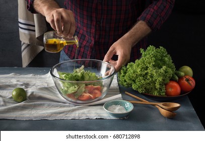 Man Cooking Vegetables Salad In Home Kitchen. Male Hands Pouring Olive Oil In Bowl With Salad