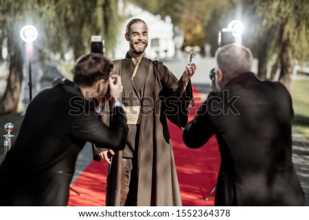 Man in costume as a well-known film character walking with annoying photo reporters on the red carpet during awards ceremony