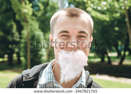 Man with cotton candy beard in the park close-up. Portrait of young 20 european eating a candy floss with smiling handsome face looking at the camera. Happiness lifestyle moments. Happy as a child.