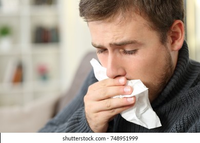 Man Coughing Covering Mouth With A Tissue Sitting On A Couch In A House Interior