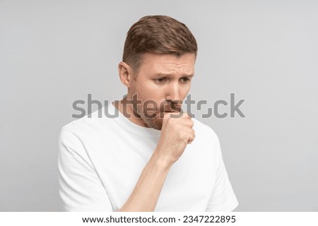 Man coughs, covering himself with fist isolated on gray. Middle aged male got sick and suffers from first symptoms of cold. Dry or wet cough, phlegm, sore throat, cold, illness, poor immunity concept.