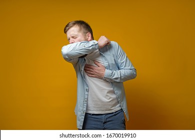 Man coughs in his elbow and holds hand on chest, experiencing pain. Concept of the spread of the virus.