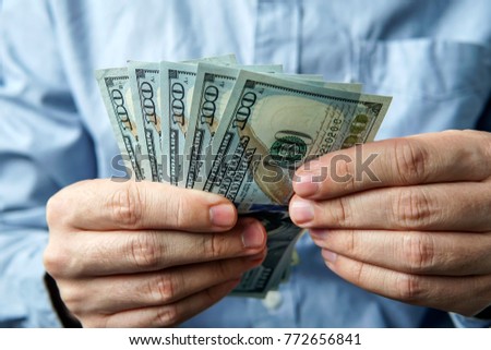 man counting five hundred US dollars. The businessman thinks of profit. Dollar bills in the hands of men on the background of blue business shirt. Success, motivation, financial flows, wealth.