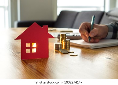 Man Counting House Price, Home Insurance Cost, Property Value Or Rent On Paper. Realtor Or Real Estate Agent Writing Offer. Mortgage, Saving And Buying Apartment. Money And Small Building On Table.