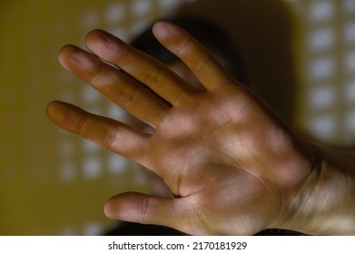 Man Covered His Face With His Hand Out In Front Of Him. Portrait Of A Middle-aged Male Against The Wall. The Light And Shadow Pattern On The Wall And The Man's Palm. Personal Space, Proxemic Concept.