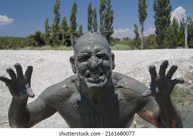 A man covered in mud makes a funny face at a river mud bath in Turkey