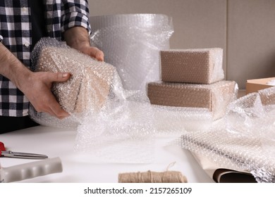 Man covering box with bubble wrap at table in warehouse, closeup