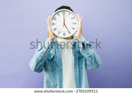 Man covering face with a clock, representing concepts of time, schedule, punctuality, and managing workload in a studio