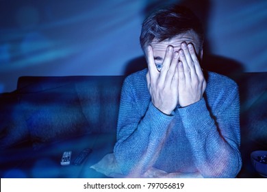 Man covering his eyes while watching TV
