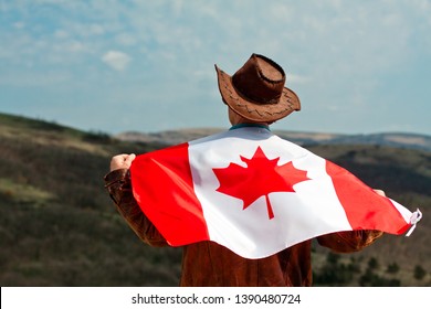 A man in a cowboy hat and a leather jacket in the mountains take canadian flag.