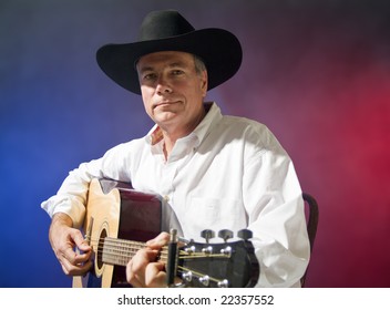 A man in a cowboy hat playing a guitar, colorful, smokey background.