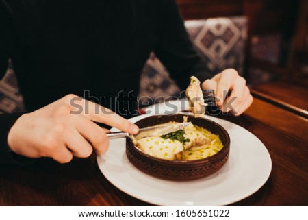 man in cozy Georgian restaurant eats dish Chkmerul chicken meat with cream sauce