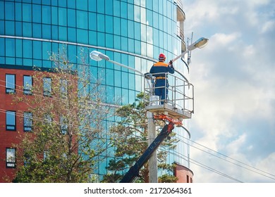 Man in cradle painting lamppost. Worker in aerial platform, man paint street light pole at height, renovation works. Worker in lift bucket at height, risky job. Paint and renovate street light