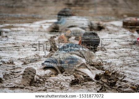 A man crawling under barbed wire in mud