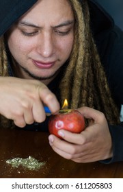 Man Creating An Apple Bong Using Knife And A Plastic Tube, Drug Addiction Concept, Marijuana Lying On Table