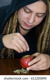 Man Creating An Apple Bong Using Knife And A Plastic Tube, Drug Addiction Concept, Marijuana Lying On Table