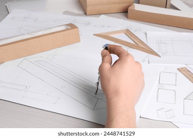 Man creating packaging design at light wooden table, closeup