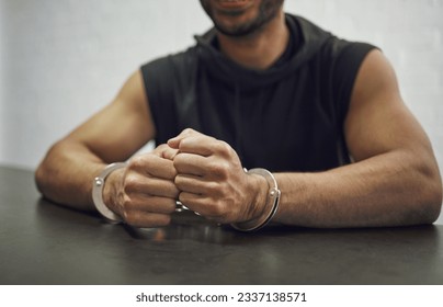 Man, criminal and handcuffs for interrogation, crime or money laundering in arrest on table in room. Closeup of male person, gangster or suspect in jail, justice or guilty for fraud, theft or scam