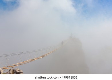 Man Crossing The Chasm On The Hanging Bridge In Fog (focus On The Middle Of Bridge)