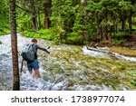 Man crossing fording river on Conundrum Creek Trail in Aspen, Colorado in 2019 summer in forest woods with strong current and deep water