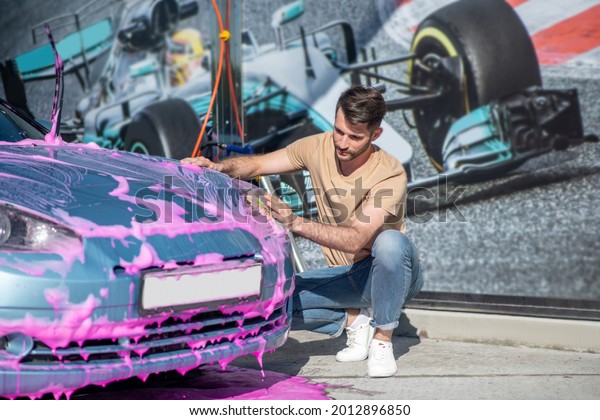 Man crouched near\
car wiping bright foam
