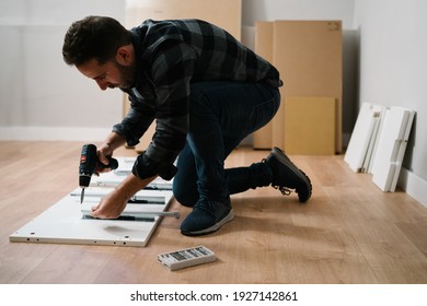 Man Crouched On The Floor Assembling A Piece Of Furniture. Do It Yourself Furniture Assembly.