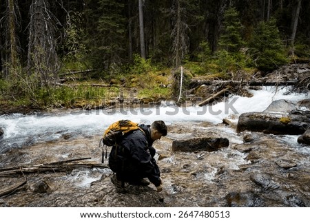 Man crouching by forest stream touching cold water