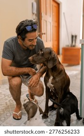 Man crouching down, affectionately looking at a brown dog surrounded by playful puppies on a patterned floor at home