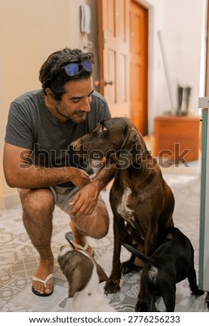 Man crouching down, affectionately looking at a brown dog surrounded by playful puppies on a patterned floor at home