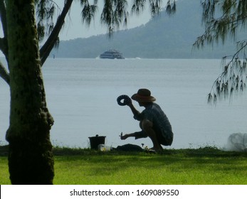 Man Crouching With Fishing Hand Line And Bucket, Cairns Harbour In Background