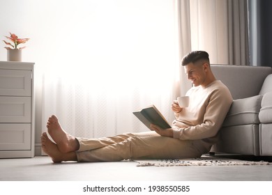 Man with cup of hot drink reading book at home. Floor heating concept - Powered by Shutterstock