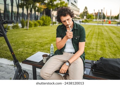 Man with curly hair sits on a park bench, lights a cigar and rests - Powered by Shutterstock