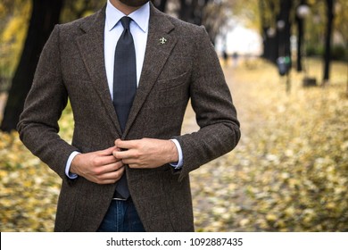 Man in custom tailored suit posing outdoors in autumn and buttoning his coat