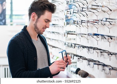 Man As Customer Choosing Glasses From Shelf In Optician Shop