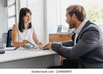 Man customer client male buyer in grey suit choose auto want buy new car automobile consult with female salesman read catalog sit at office in showroom salon dealership store indoor. Sale concept.