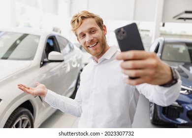 Man Customer Happy Buyer Client In White Shirt Do Selfie Shot On Mobile Cell Phone Show Car Choose Auto Want Buy New Automobile In Showroom Vehicle Dealership Store Motor Show Indoor. Sales Concept.