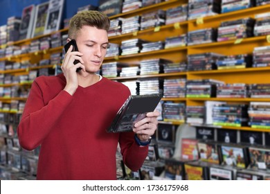 Man Customer Talking By Phone Near Shelves With Large Collection Of DVDs In Store