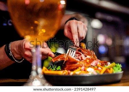 man cuts a pork knuckle with a knife and fork