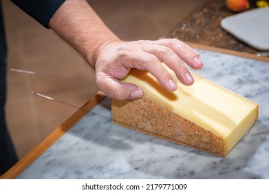 A Man Cuts A Portion Of The Gruyère With A Wire, The Famous Swiss Cheese In A Cellar On A Marbble Background